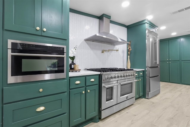 kitchen with wall chimney exhaust hood, high quality appliances, light wood-type flooring, and green cabinetry