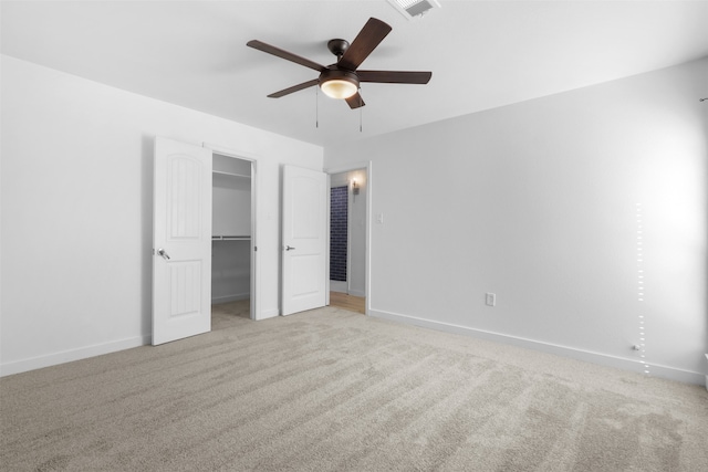 unfurnished bedroom with light carpet, a walk in closet, a closet, and ceiling fan