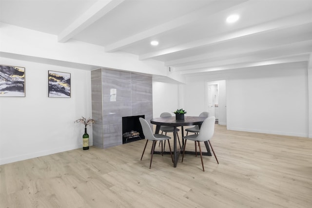 dining space featuring beam ceiling, light hardwood / wood-style flooring, and a tiled fireplace