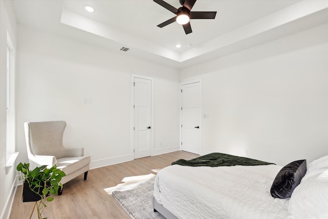 bedroom featuring ceiling fan, light hardwood / wood-style floors, and a tray ceiling