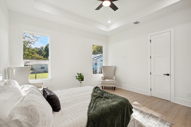 bedroom with multiple windows, light wood-type flooring, a tray ceiling, and ceiling fan