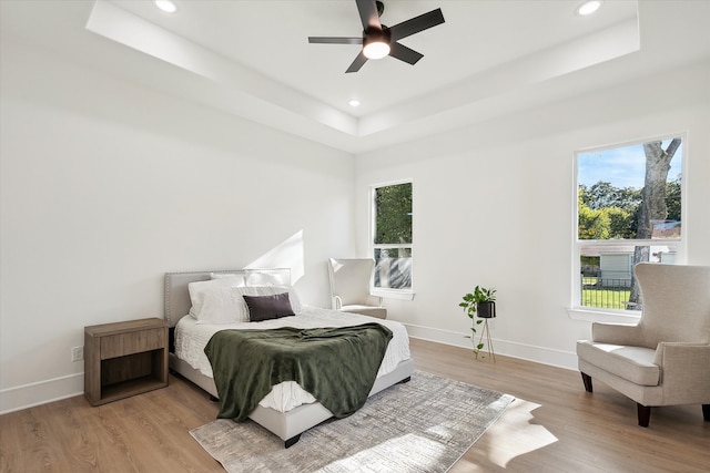 bedroom featuring ceiling fan, light hardwood / wood-style floors, and a tray ceiling