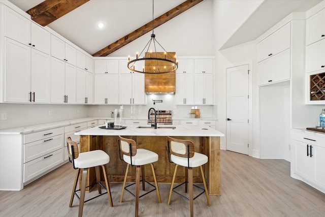 kitchen featuring beam ceiling, a breakfast bar, an island with sink, and light wood-type flooring