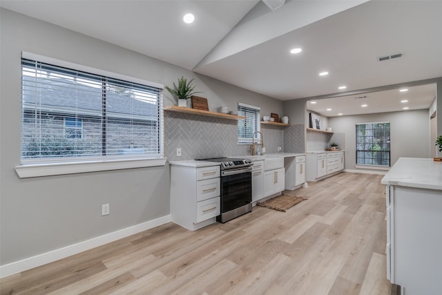 kitchen featuring stainless steel electric stove, light hardwood / wood-style floors, white cabinetry, and backsplash