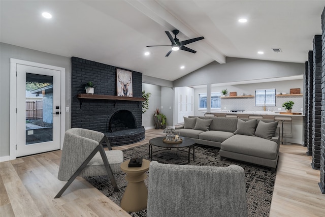 living room with a fireplace, lofted ceiling with beams, light hardwood / wood-style flooring, and a healthy amount of sunlight