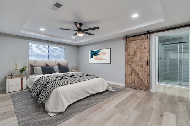 bedroom featuring ceiling fan, a barn door, light hardwood / wood-style floors, and a tray ceiling