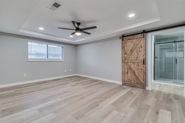 spare room featuring ceiling fan, a barn door, light wood-type flooring, and a tray ceiling