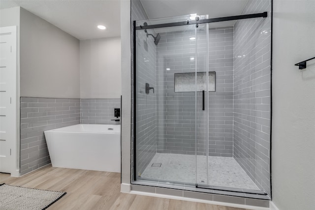 bathroom with wood-type flooring, tile walls, and independent shower and bath