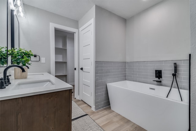 bathroom featuring a textured ceiling, vanity, hardwood / wood-style flooring, tile walls, and a bathing tub