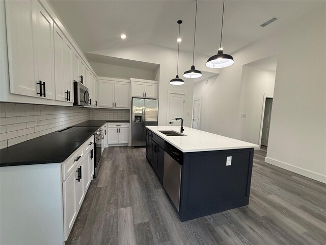 kitchen with appliances with stainless steel finishes, a kitchen island with sink, sink, decorative light fixtures, and white cabinetry