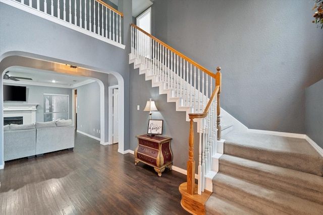 stairs with a high ceiling, wood-type flooring, a healthy amount of sunlight, and ceiling fan