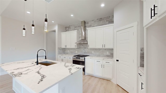 kitchen featuring stainless steel range with gas cooktop, sink, hanging light fixtures, wall chimney range hood, and an island with sink