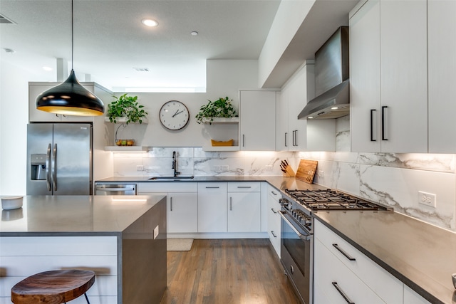 kitchen featuring appliances with stainless steel finishes, wall chimney range hood, sink, pendant lighting, and white cabinetry