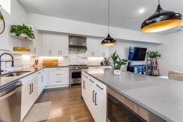 kitchen with appliances with stainless steel finishes, sink, white cabinetry, and wall chimney range hood