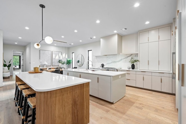 kitchen featuring white cabinetry, sink, light hardwood / wood-style flooring, a large island with sink, and pendant lighting