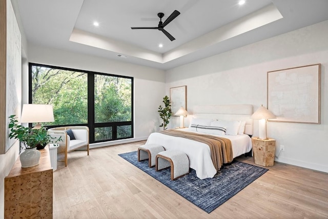 bedroom featuring ceiling fan, light hardwood / wood-style floors, and a tray ceiling