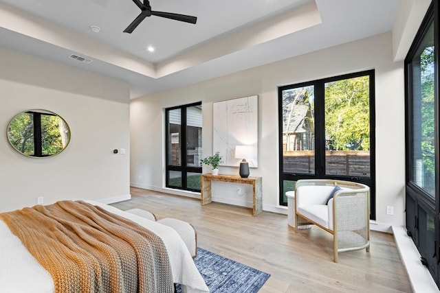 bedroom with ceiling fan, a tray ceiling, and light hardwood / wood-style flooring