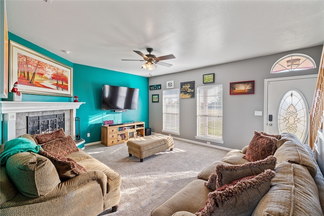 living room featuring a tiled fireplace, light carpet, ceiling fan, and a textured ceiling