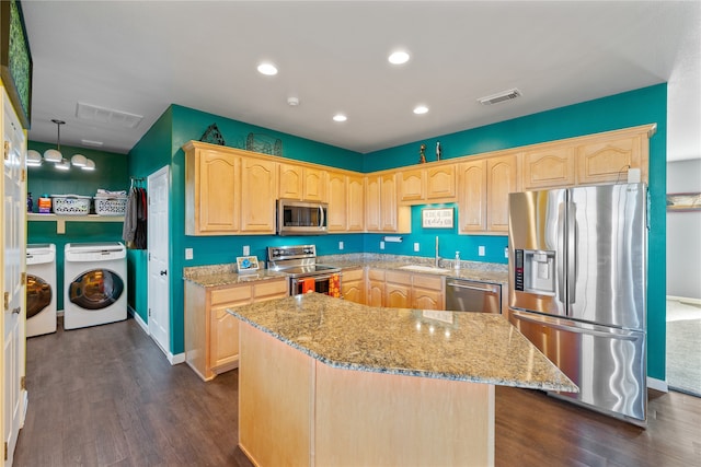 kitchen with washer and clothes dryer, a kitchen island, dark wood-type flooring, and appliances with stainless steel finishes