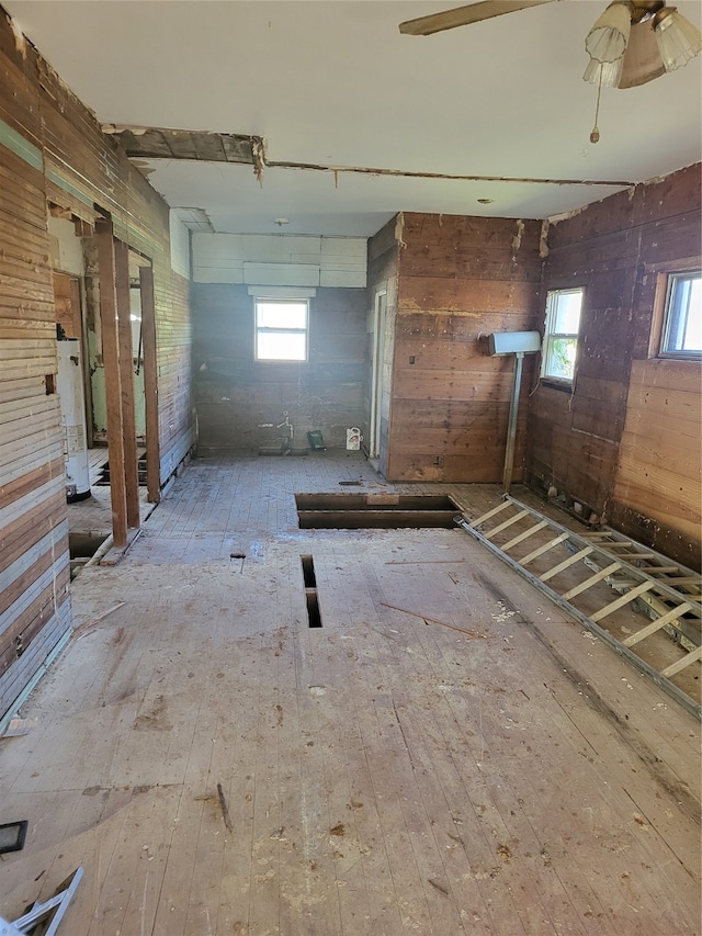 interior space with ceiling fan, water heater, wood walls, and light wood-type flooring