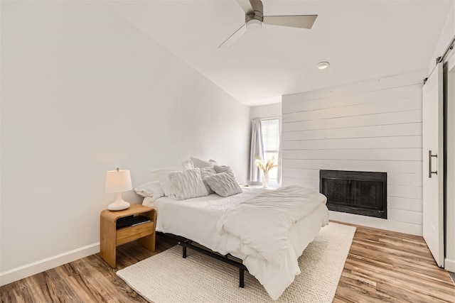 bedroom with ceiling fan, a barn door, light hardwood / wood-style flooring, a fireplace, and lofted ceiling