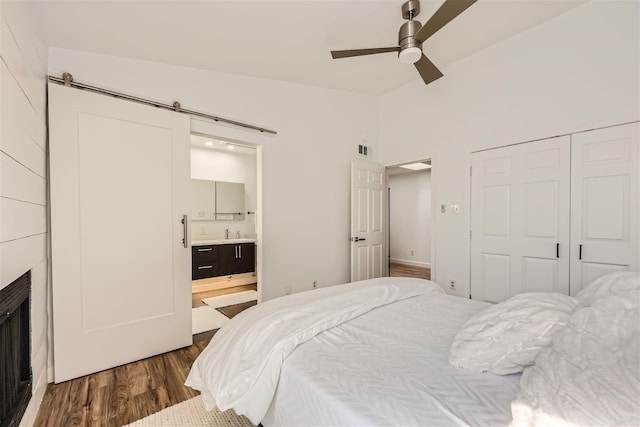 bedroom featuring connected bathroom, ceiling fan, sink, dark wood-type flooring, and a barn door