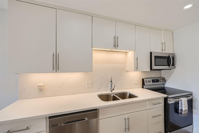 kitchen with white cabinetry, sink, light stone counters, decorative backsplash, and appliances with stainless steel finishes