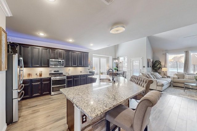 kitchen with a kitchen breakfast bar, an island with sink, appliances with stainless steel finishes, and light hardwood / wood-style flooring