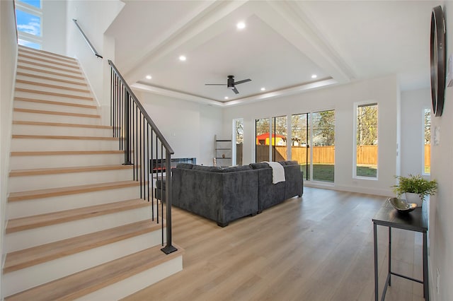 living room featuring ceiling fan, light hardwood / wood-style floors, and a tray ceiling