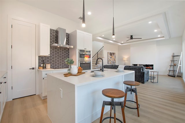 kitchen featuring a center island with sink, wall chimney range hood, and double oven