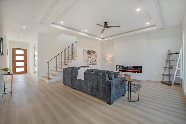 living room with light hardwood / wood-style floors, a raised ceiling, and ceiling fan