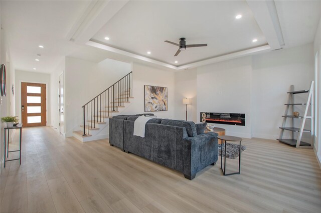 living room with light hardwood / wood-style floors, a raised ceiling, and ceiling fan