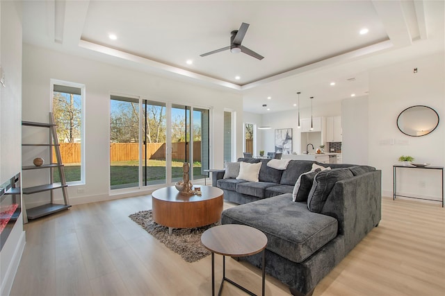 living room featuring ceiling fan, light hardwood / wood-style floors, a raised ceiling, and plenty of natural light