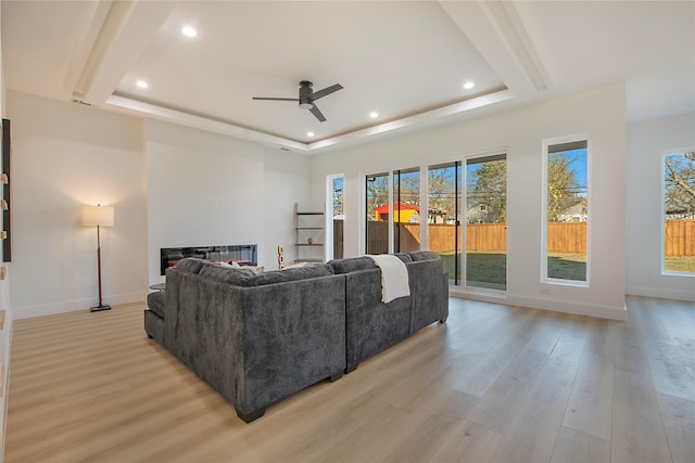 living room with a raised ceiling, ceiling fan, and light hardwood / wood-style flooring