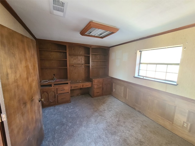 unfurnished office featuring dark colored carpet, built in shelves, built in desk, and crown molding