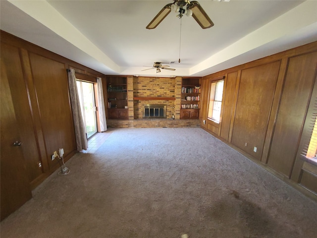 unfurnished living room featuring light carpet, a raised ceiling, a brick fireplace, and wood walls