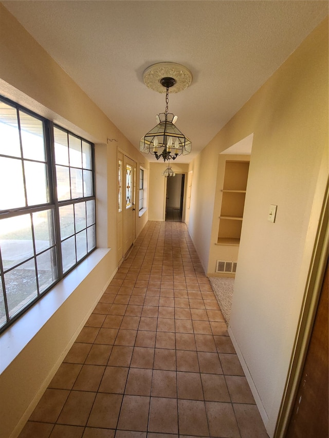 corridor with tile patterned flooring, built in shelves, a textured ceiling, and an inviting chandelier