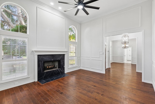 unfurnished living room featuring ornamental molding, dark hardwood / wood-style floors, a wealth of natural light, a premium fireplace, and ceiling fan with notable chandelier