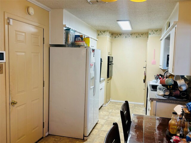 kitchen featuring a textured ceiling, sink, white refrigerator with ice dispenser, white cabinetry, and black oven