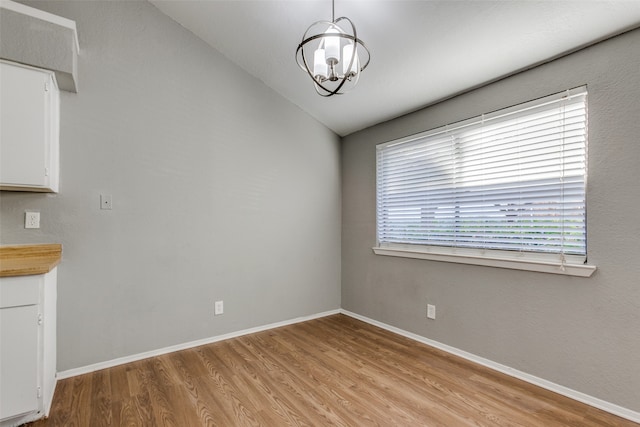 unfurnished dining area featuring light wood-type flooring, lofted ceiling, and a notable chandelier