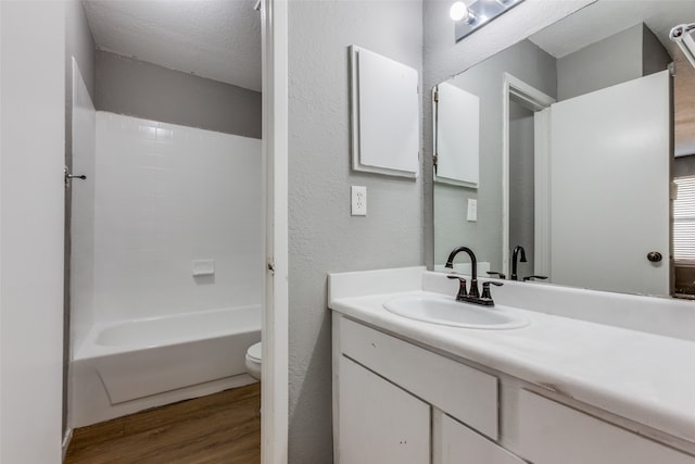 full bathroom with washtub / shower combination, wood-type flooring, a textured ceiling, toilet, and vanity