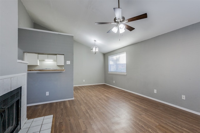 unfurnished living room with hardwood / wood-style flooring, ceiling fan, lofted ceiling, and a tile fireplace