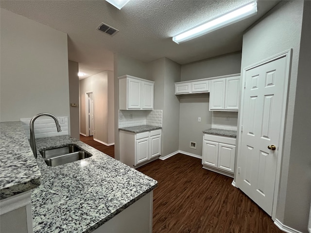 kitchen featuring kitchen peninsula, light stone counters, white cabinetry, and sink