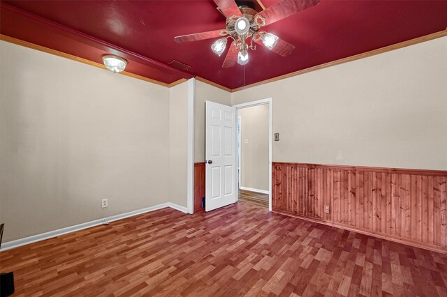 spare room featuring wood-type flooring, wooden walls, ceiling fan, and ornamental molding