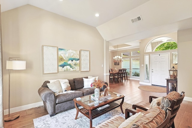 living room with hardwood / wood-style floors, an inviting chandelier, and vaulted ceiling