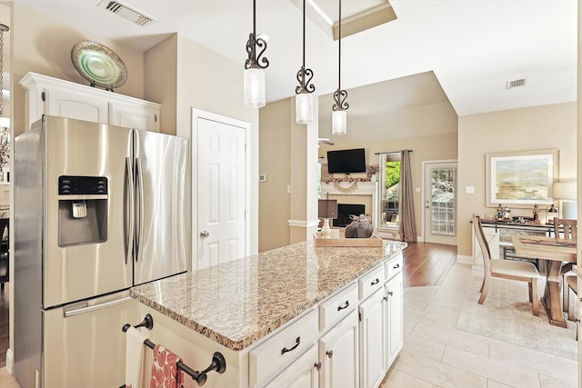 kitchen featuring stainless steel refrigerator with ice dispenser, light stone countertops, decorative light fixtures, a kitchen island, and white cabinetry