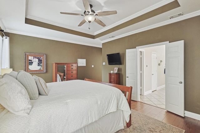 bedroom featuring wood-type flooring, a raised ceiling, ceiling fan, and crown molding