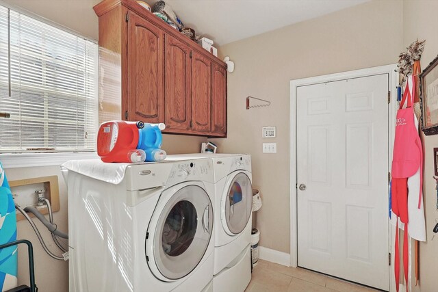 clothes washing area featuring separate washer and dryer, light tile patterned floors, and cabinets