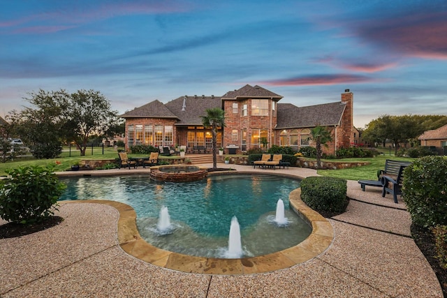 pool at dusk featuring a pool with connected hot tub and a patio