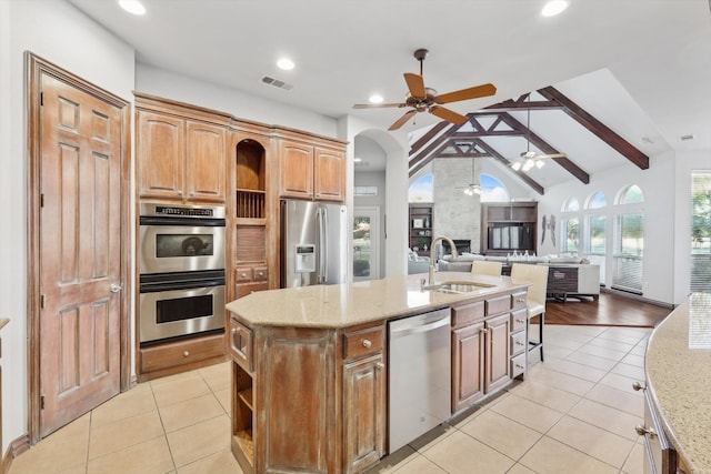 kitchen featuring sink, vaulted ceiling with beams, an island with sink, light tile patterned floors, and appliances with stainless steel finishes